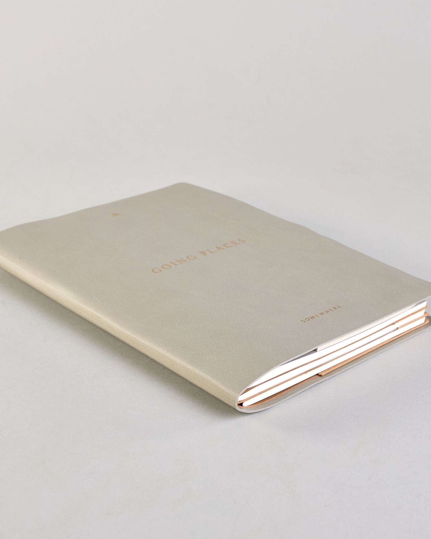 Hellgraues PU-Notizbuch mit zarter goldener Aufschrift "Going Places" auf der Vorderseite. Innen ist das System aus Kraftpapier und es können drei Hefte und ein Block flexibel eingehängt und immer wieder ausgetauscht werden. #2