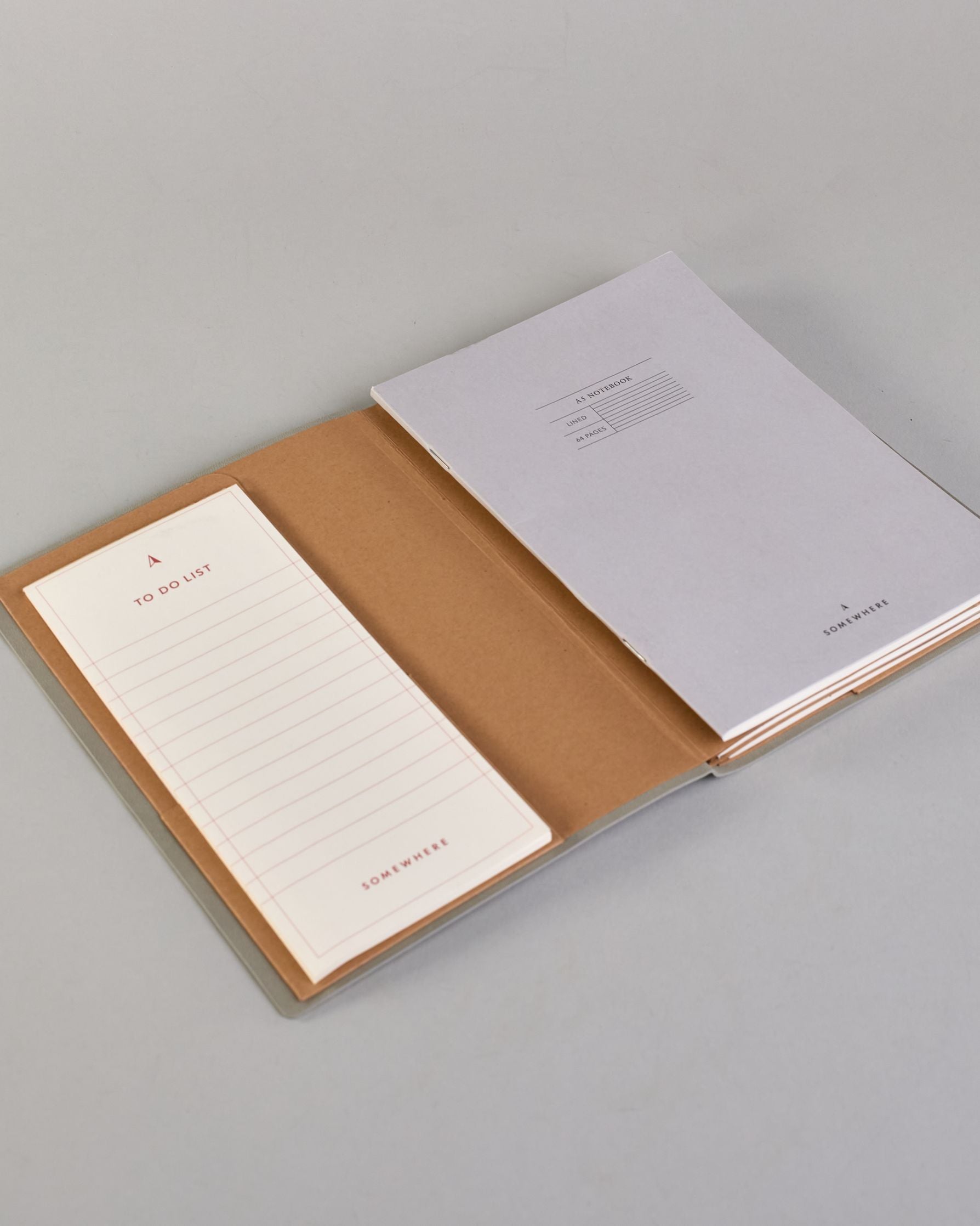 Hellgraues PU-Notizbuch mit zarter goldener Aufschrift "Going Places" auf der Vorderseite. Innen ist das System aus Kraftpapier und es können drei Hefte und ein Block flexibel eingehängt und immer wieder ausgetauscht werden. #3