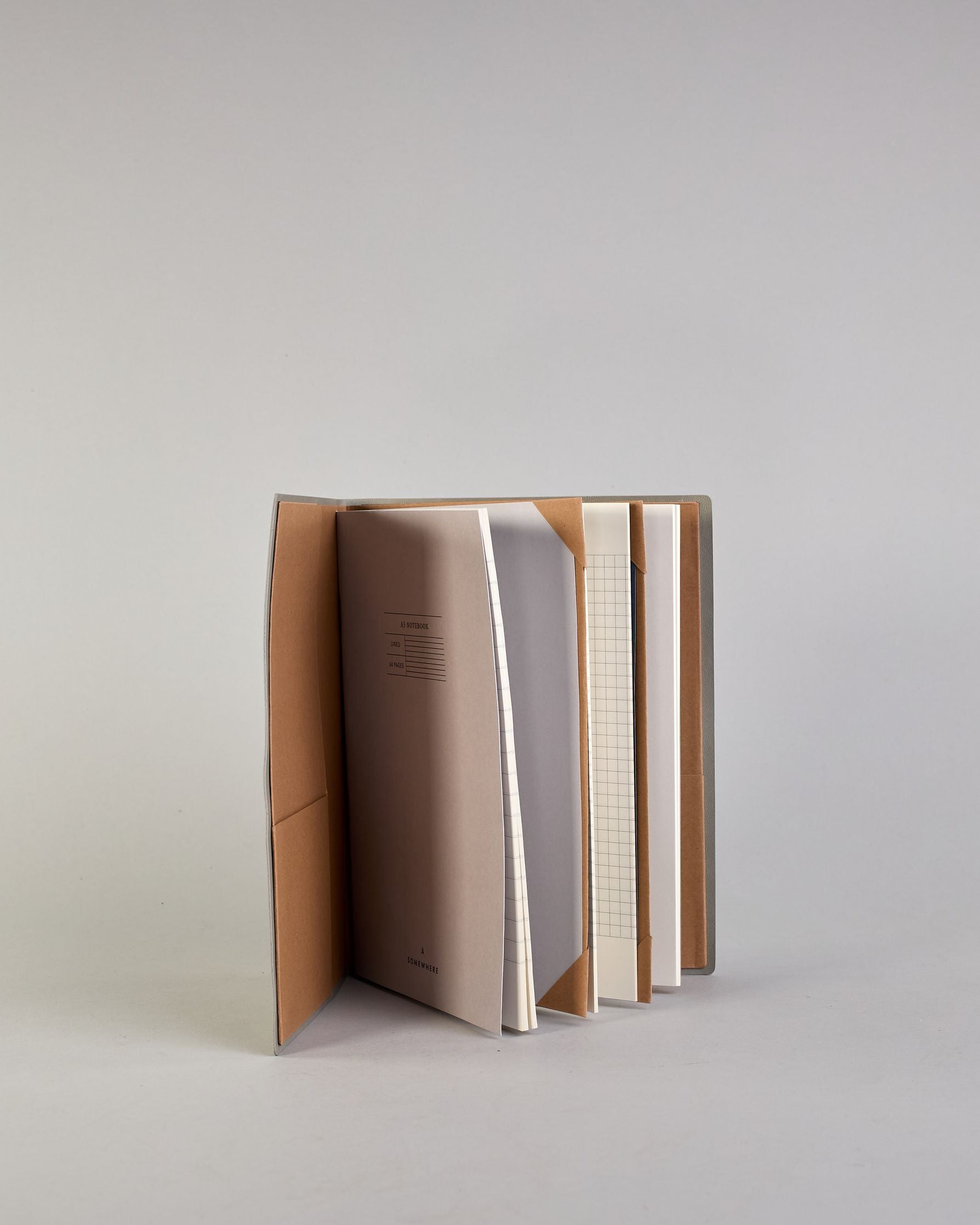 Hellgraues PU-Notizbuch mit zarter goldener Aufschrift "Going Places" auf der Vorderseite. Innen ist das System aus Kraftpapier und es können drei Hefte und ein Block flexibel eingehängt und immer wieder ausgetauscht werden. #7