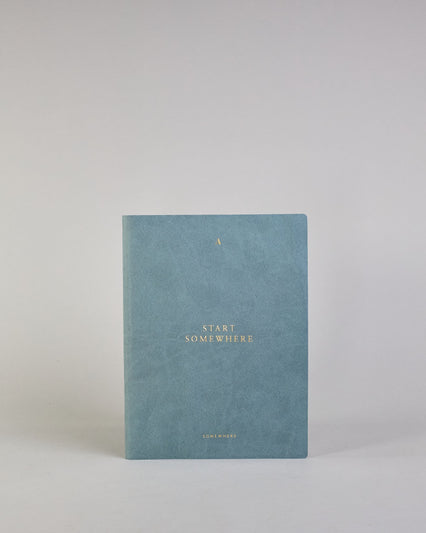 Jeansblaues PU-Notizbuch mit zarter goldener Aufschrift "Start Somewhere" auf der Vorderseite. Innen ist das System aus Kraftpapier und es können drei Hefte und ein Block flexibel eingehängt und immer wieder ausgetauscht werden. #1