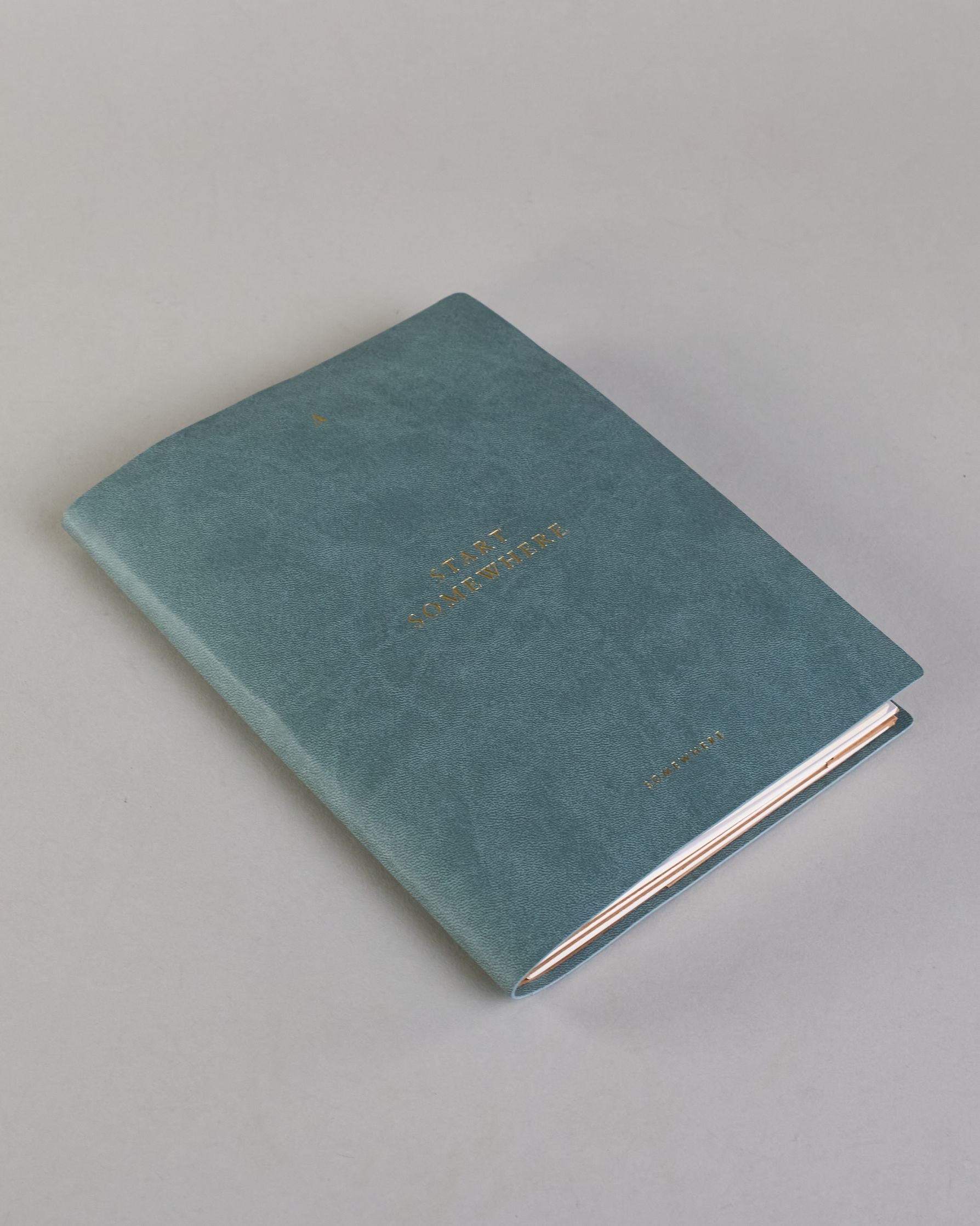 Jeansblaues PU-Notizbuch mit zarter goldener Aufschrift "Start Somewhere" auf der Vorderseite. Innen ist das System aus Kraftpapier und es können drei Hefte und ein Block flexibel eingehängt und immer wieder ausgetauscht werden. #2