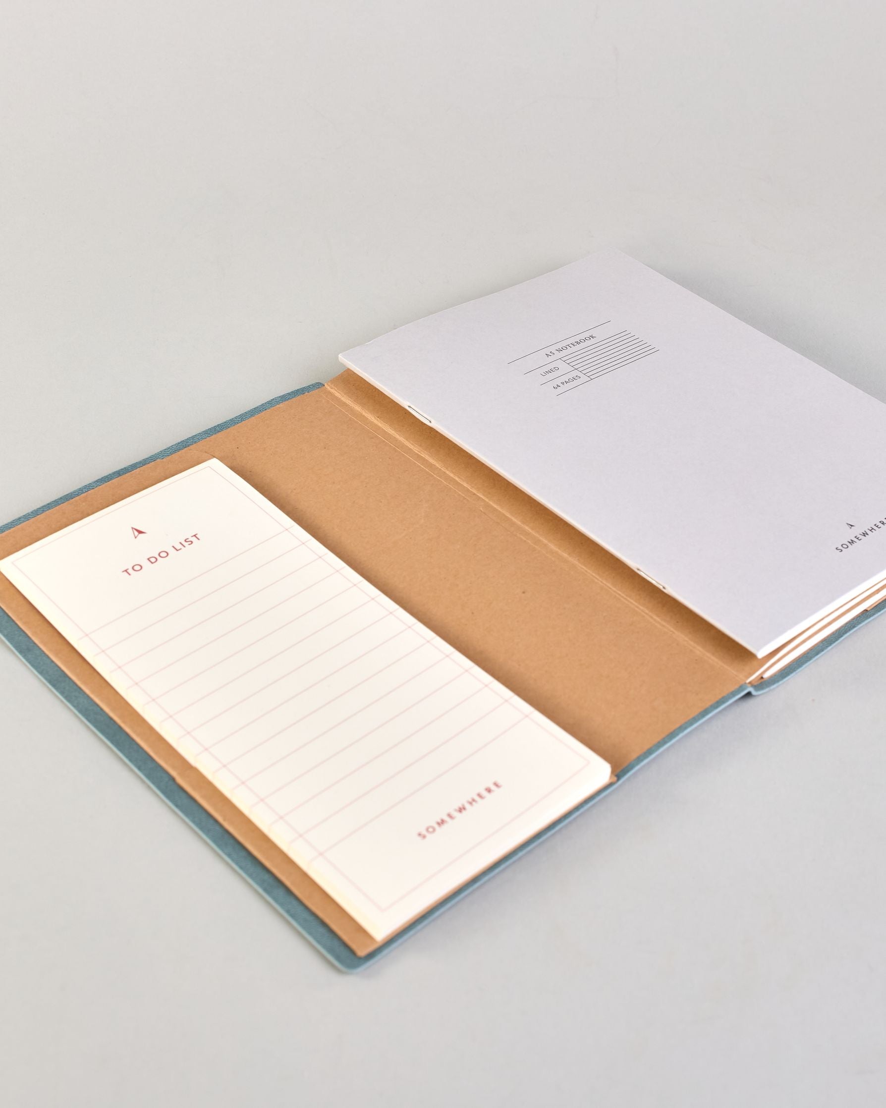 Jeansblaues PU-Notizbuch mit zarter goldener Aufschrift "Start Somewhere" auf der Vorderseite. Innen ist das System aus Kraftpapier und es können drei Hefte und ein Block flexibel eingehängt und immer wieder ausgetauscht werden. #3