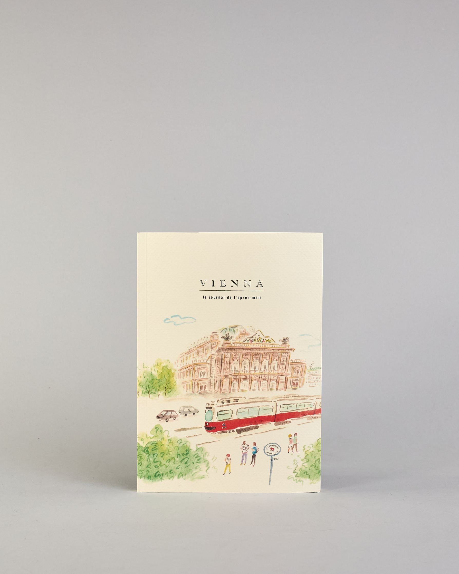 Notizbuch mit cremefarbenem Einband, darauf eine zarte Illustration der Wiener Staatsoper mit vorbeifahrender Straßenbahn und kleinen Figuren im Vordergrund. Titel: ‚Vienna – le journal de l’après-midi. Innen ist jede Seite individuell illustriert. #1