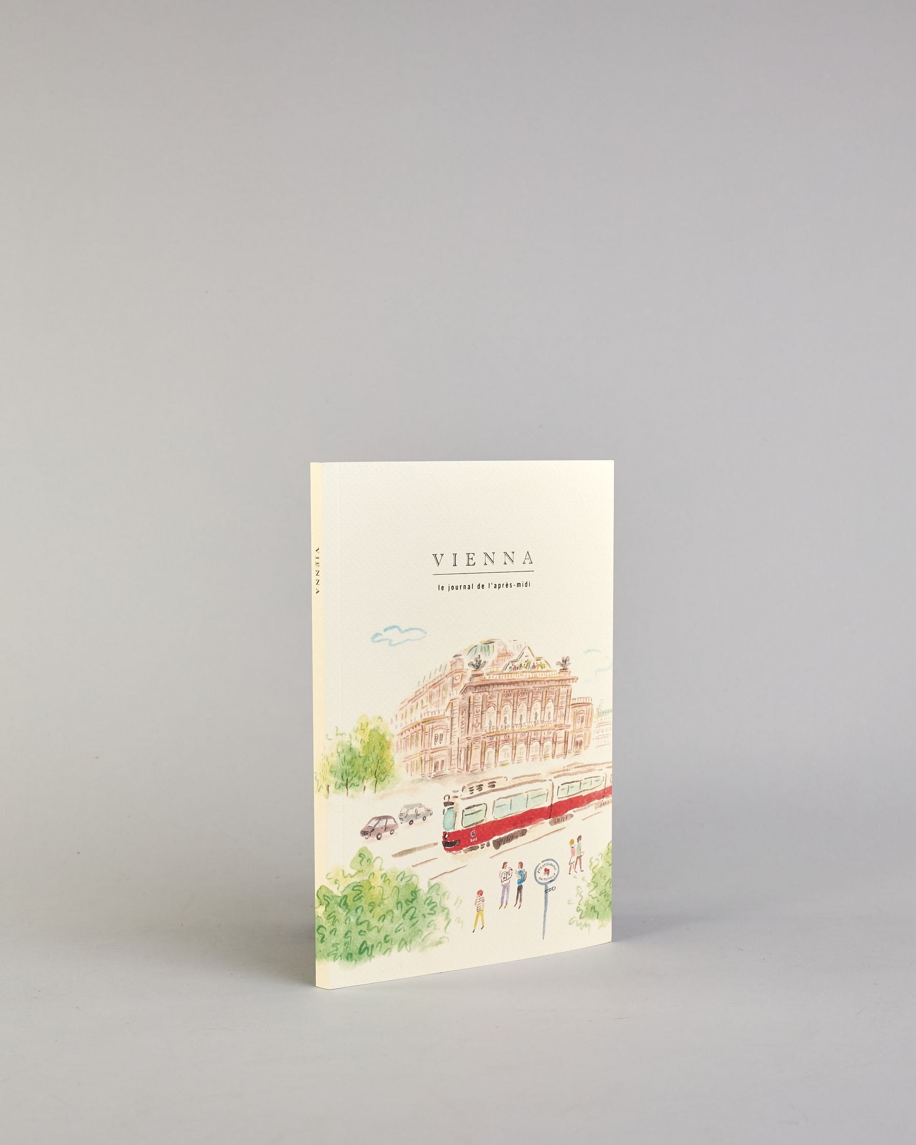Notizbuch mit cremefarbenem Einband, darauf eine zarte Illustration der Wiener Staatsoper mit vorbeifahrender Straßenbahn und kleinen Figuren im Vordergrund. Titel: ‚Vienna – le journal de l’après-midi. Innen ist jede Seite individuell illustriert. #2