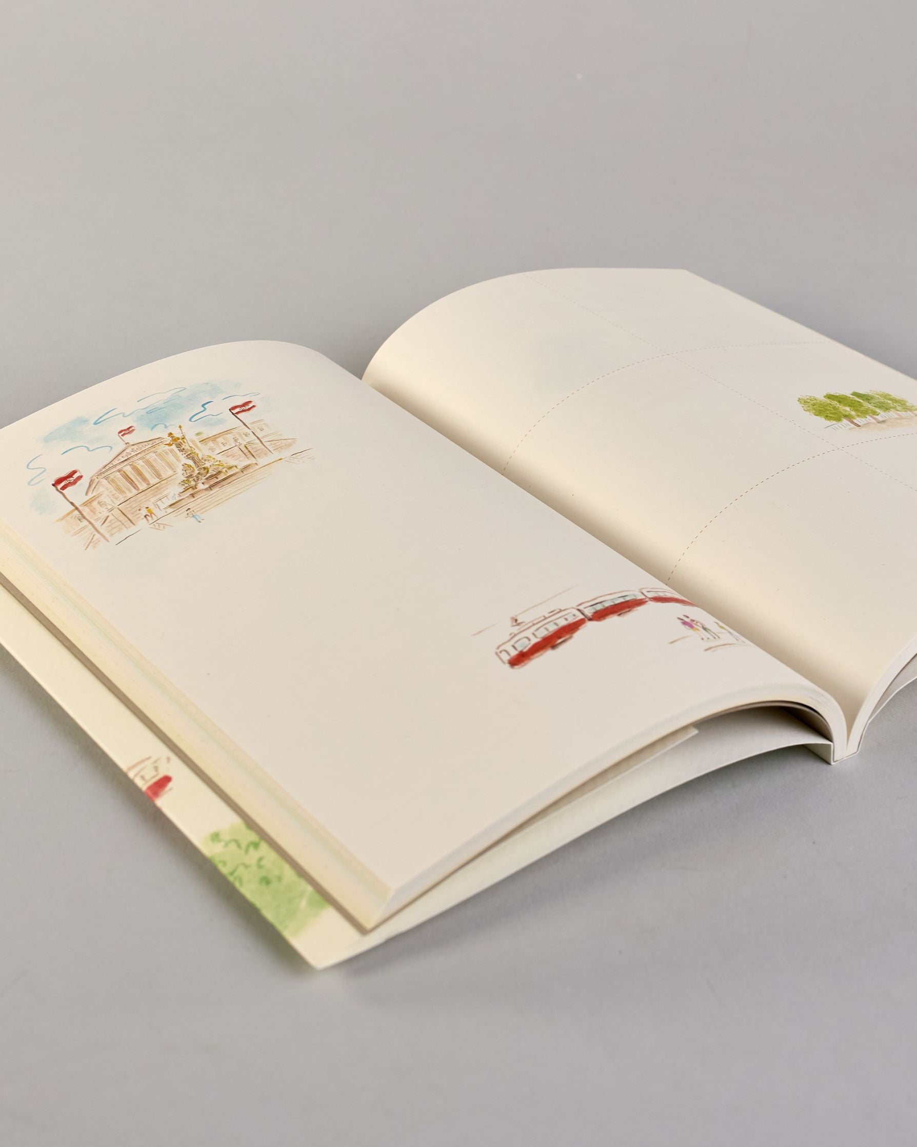 Notizbuch mit cremefarbenem Einband, darauf eine zarte Illustration der Wiener Staatsoper mit vorbeifahrender Straßenbahn und kleinen Figuren im Vordergrund. Titel: ‚Vienna – le journal de l’après-midi. Innen ist jede Seite individuell illustriert. #4