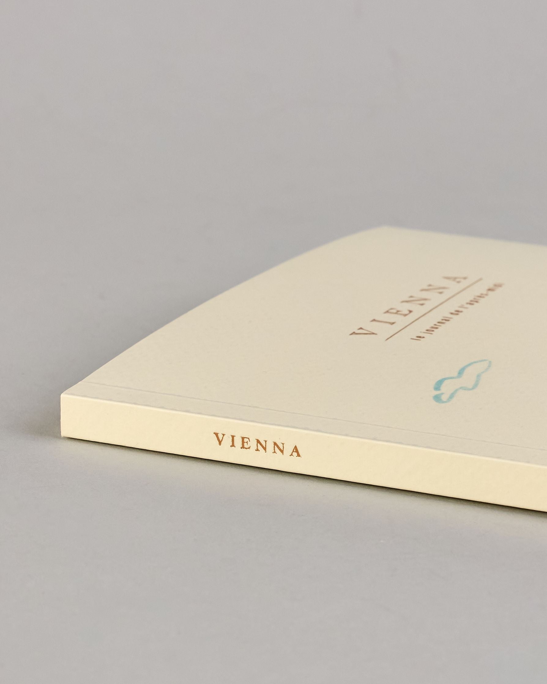 Notizbuch mit cremefarbenem Einband, darauf eine zarte Illustration der Wiener Staatsoper mit vorbeifahrender Straßenbahn und kleinen Figuren im Vordergrund. Titel: ‚Vienna – le journal de l’après-midi. Innen ist jede Seite individuell illustriert. #8