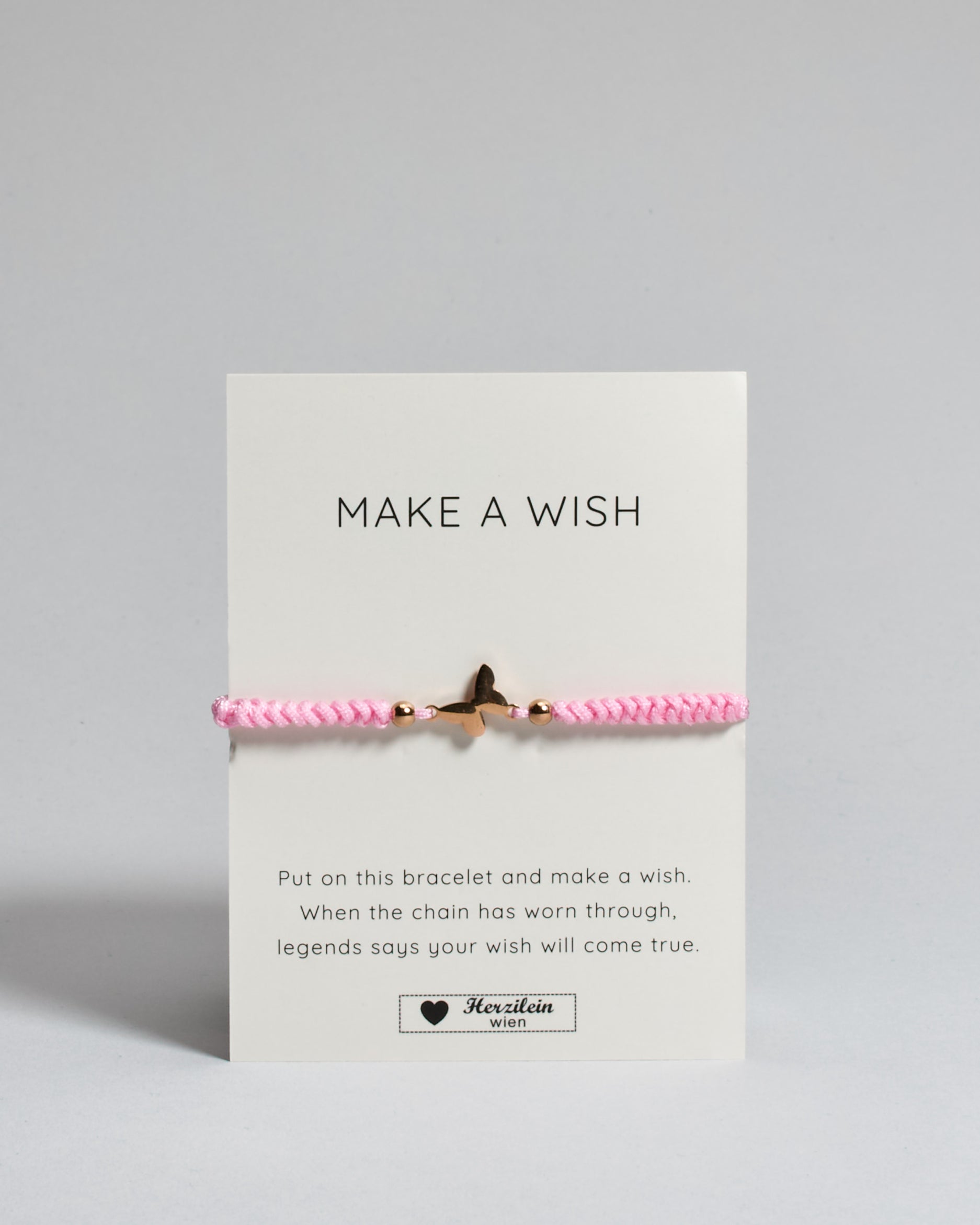 Rosa Armband mit rosé Schmetterlingsanhänger. Kommt auf einer Karte auf der oben "Make a wish" und unten "Put on this bracelet and make a wish. When the chain has worn through, legends say your wish will come true". 