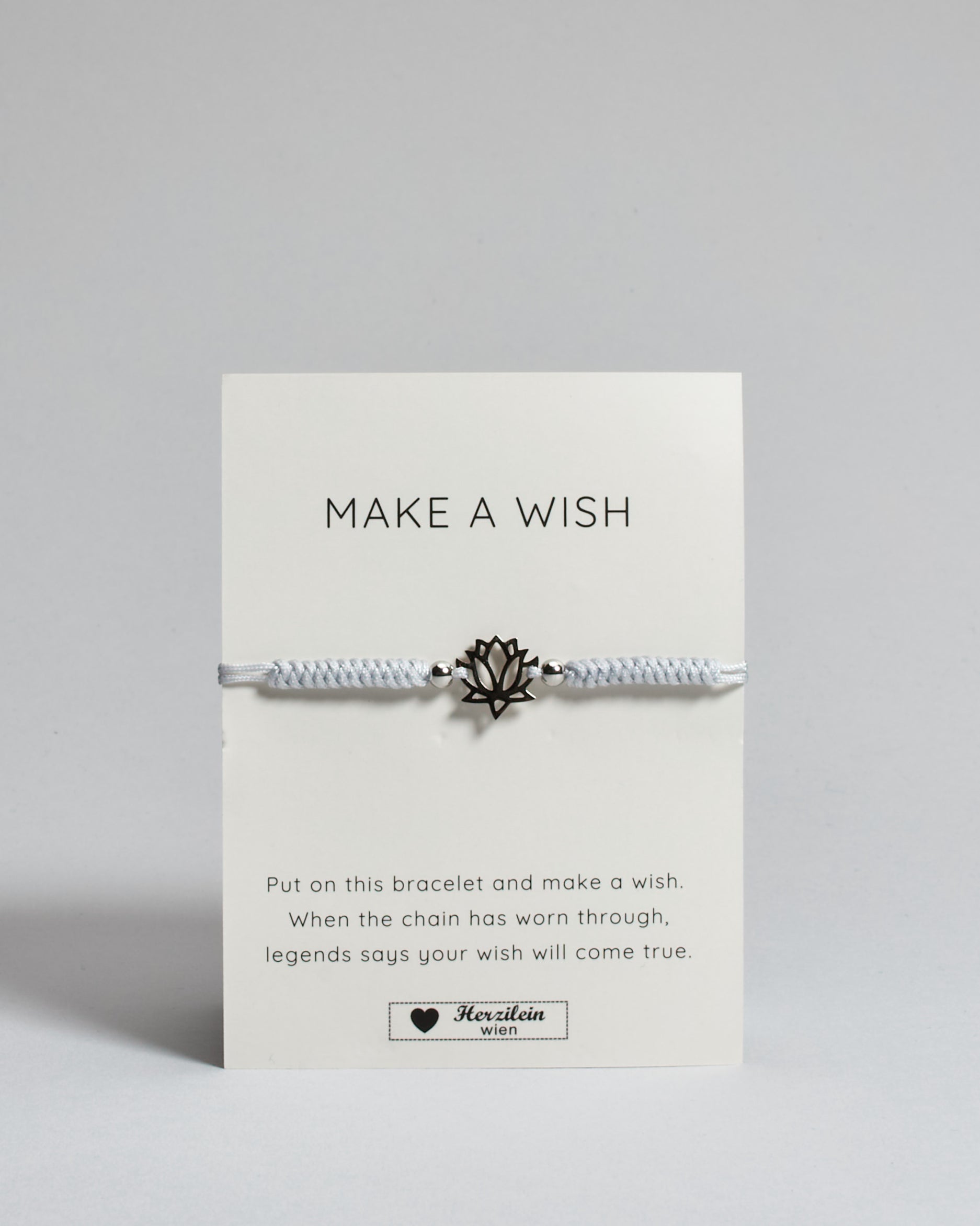Hellgraues Armband mit silber Lotusanhänger. Kommt auf einer Karte auf der oben "Make a wish" und unten "Put on this bracelet and make a wish. When the chain has worn through, legends say your wish will come true". 