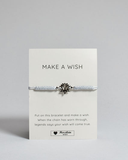 Hellgraues Armband mit silber Lotusanhänger. Kommt auf einer Karte auf der oben "Make a wish" und unten "Put on this bracelet and make a wish. When the chain has worn through, legends say your wish will come true". 