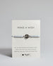 Hellgraues Armband mit silber Lotusanhänger. Kommt auf einer Karte auf der oben "Make a wish" und unten "Put on this bracelet and make a wish. When the chain has worn through, legends say your wish will come true". 