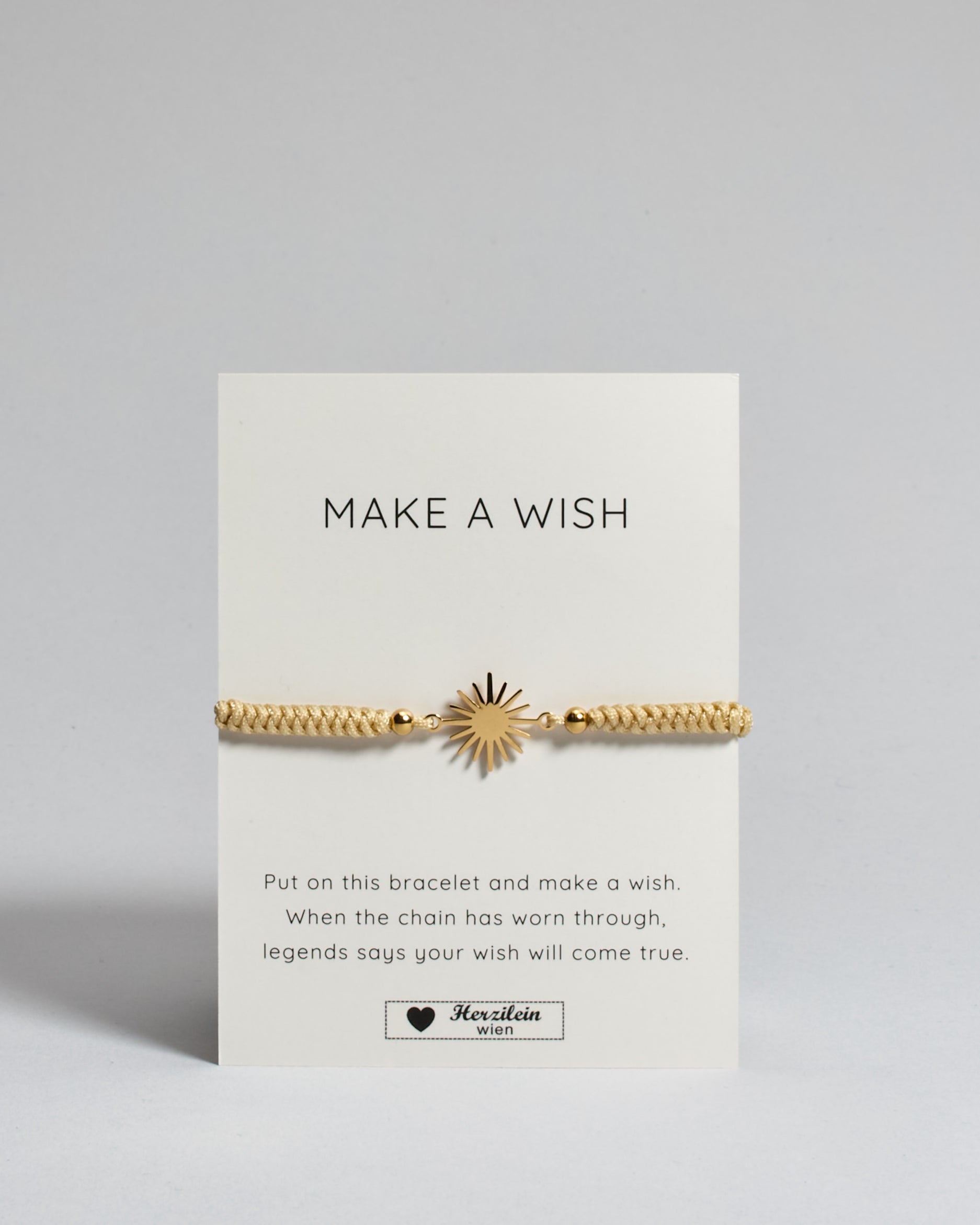 Goldenes Armband mit goldenem Sonnenanhänger. Kommt auf einer Karte auf der oben "Make a wish" und unten "Put on this bracelet and make a wish. When the chain has worn through, legends say your wish will come true". 