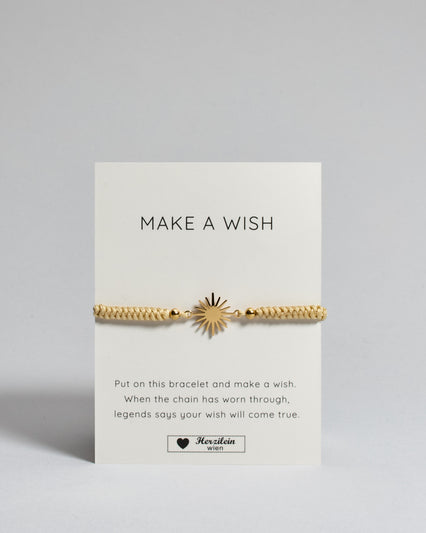 Goldenes Armband mit goldenem Sonnenanhänger. Kommt auf einer Karte auf der oben "Make a wish" und unten "Put on this bracelet and make a wish. When the chain has worn through, legends say your wish will come true". 