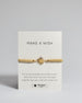 Goldenes Armband mit goldenem Sonnenanhänger. Kommt auf einer Karte auf der oben "Make a wish" und unten "Put on this bracelet and make a wish. When the chain has worn through, legends say your wish will come true". 