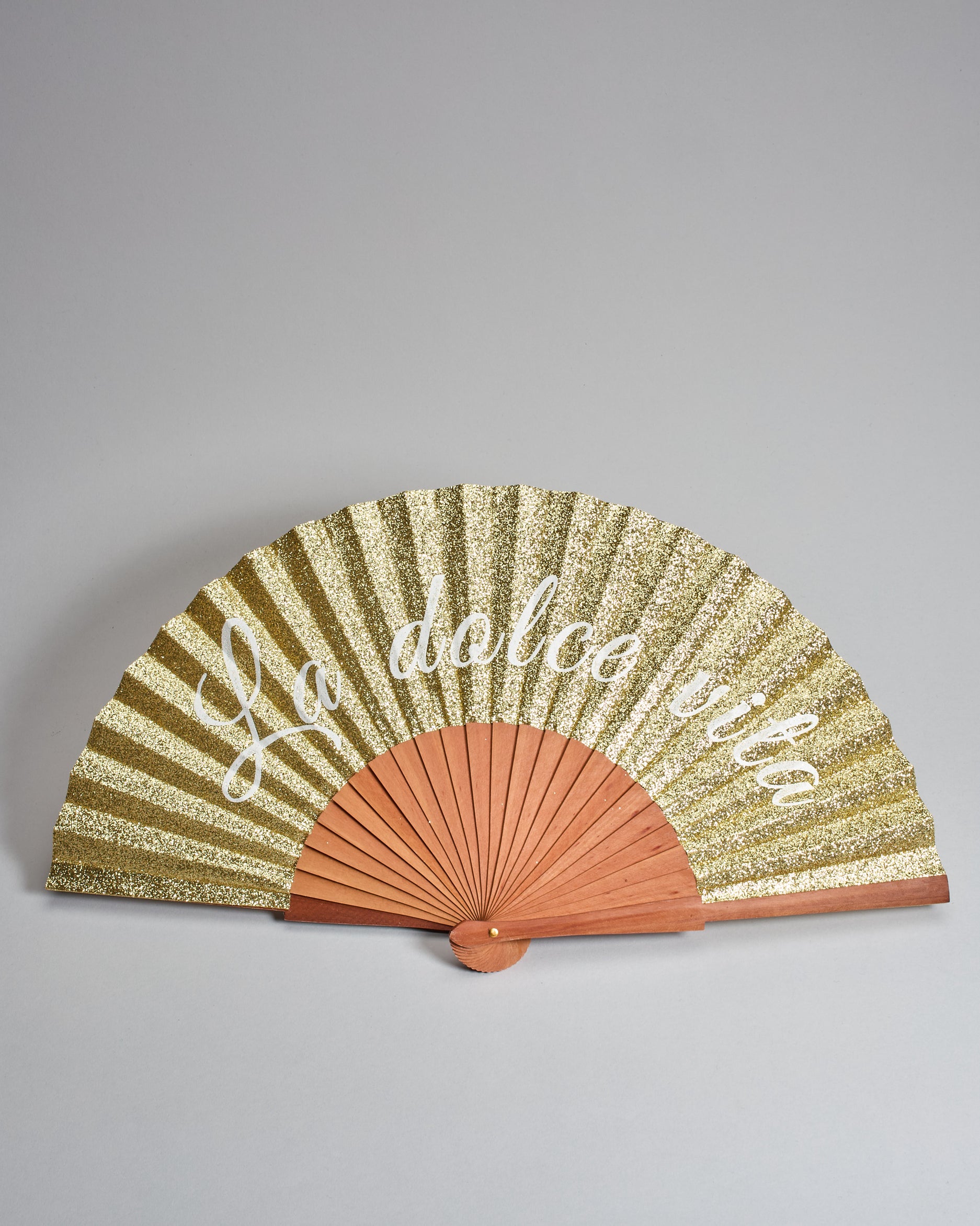 Fächer aus geöltem Holz mit Glitzer-Bespannung in gold. Es steht groß "La dolce vita" drauf. 