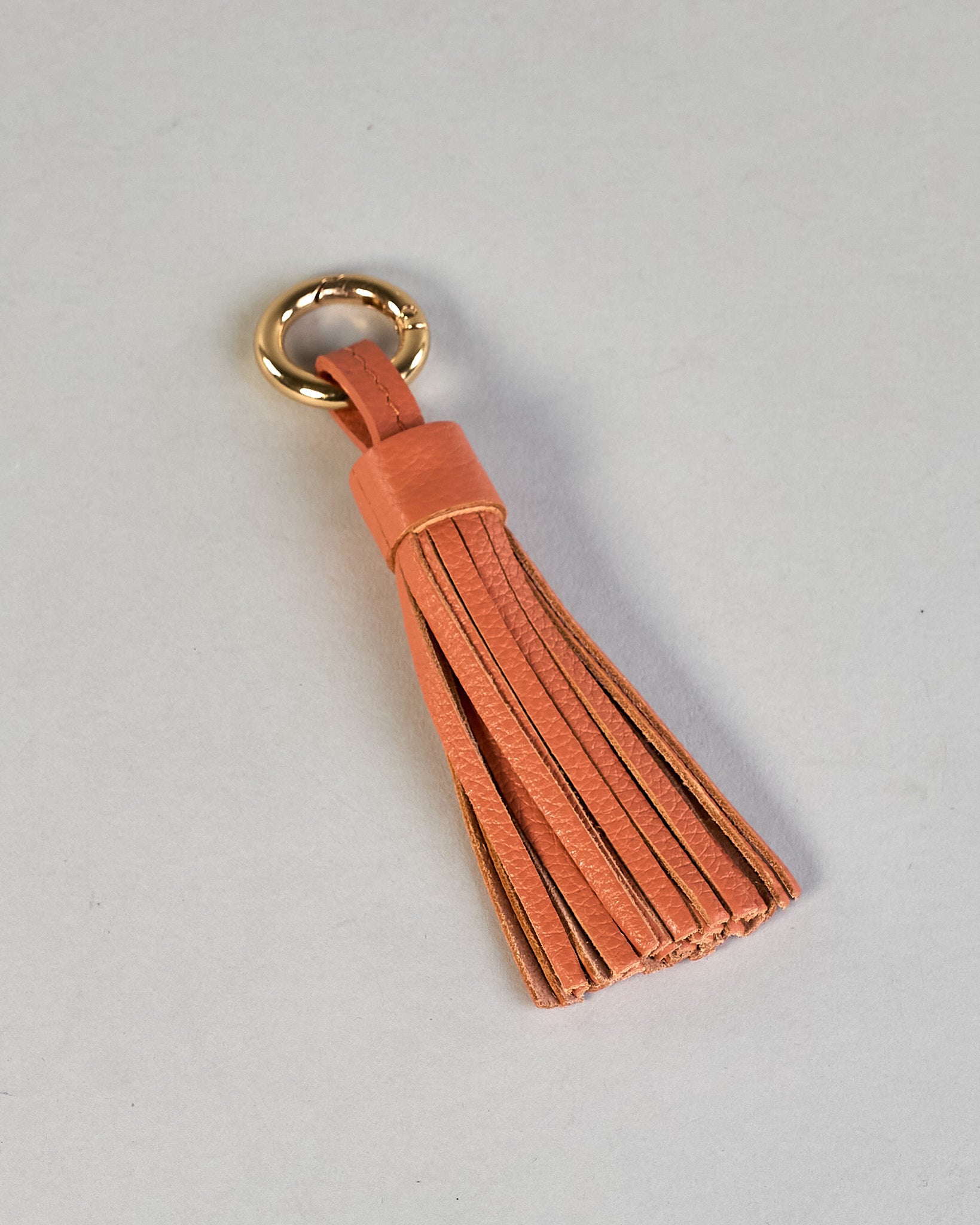 Schlüsselanhänger in Quastenform aus echtem Rindsleder. Das Leder ist orange, der Ring mit dem man das Lederaccessoire an Schlüssel oder Tasche befestigen kann ist gold.