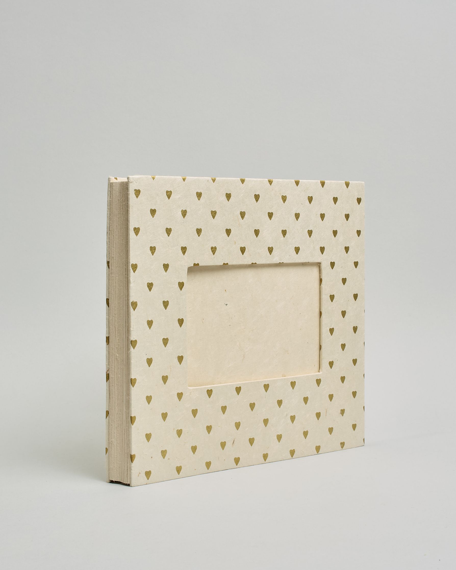 Ein Quadratisches Fotoalbum oder Gästebuch mit Hardcover in naturweißer Grundfarbe und darauf goldene kleine Herzen, die über das ganze Cover verteilt sind. In der Mitte befindet sich ein rechteckeiges Fenster hinter dem man ein Einlageblatt mit kalligrafiertem Text befestigen kann. #1