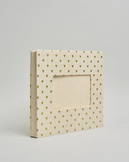Ein Quadratisches Fotoalbum oder Gästebuch mit Hardcover in naturweißer Grundfarbe und darauf goldene kleine Herzen, die über das ganze Cover verteilt sind. In der Mitte befindet sich ein rechteckeiges Fenster hinter dem man ein Einlageblatt mit kalligrafiertem Text befestigen kann. #1