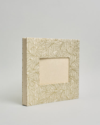 Ein Quadratisches Fotoalbum oder Gästebuch mit Hardcover in naturweißer Grundfarbe und darauf goldene Blätter, die über das ganze Cover verteilt sind. In der Mitte befindet sich ein rechteckeiges Fenster hinter dem man ein Einlageblatt mit kalligrafiertem Text befestigen kann. #1