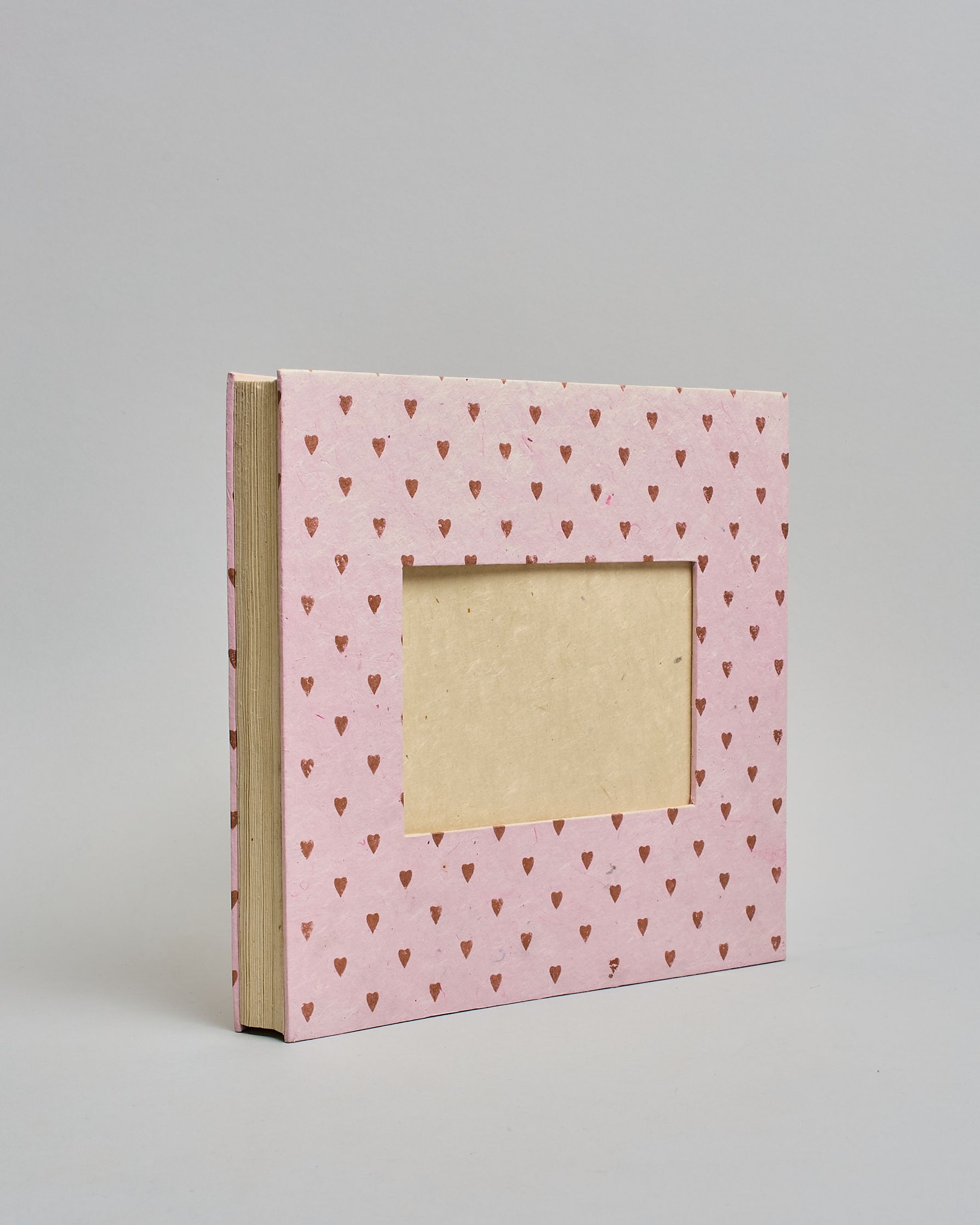 Ein Quadratisches Fotoalbum oder Gästebuch mit Hardcover in rosaner Grundfarbe und darauf roséfarbene kleinen Herzen, die über das ganze Cover verteilt sind. In der Mitte befindet sich ein rechteckeiges Fenster hinter dem man ein Einlageblatt mit kalligrafiertem Text befestigen kann. #1