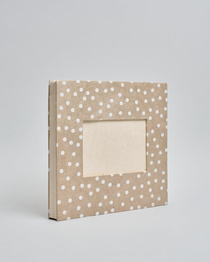Ein Quadratisches Fotoalbum oder Gästebuch mit Hardcover in beiger Grundfarbe und darauf weiße Punkte, die über das ganze Cover verteilt sind. In der Mitte befindet sich ein rechteckeiges Fenster hinter dem man ein Einlageblatt mit kalligrafiertem Text befestigen kann. #1