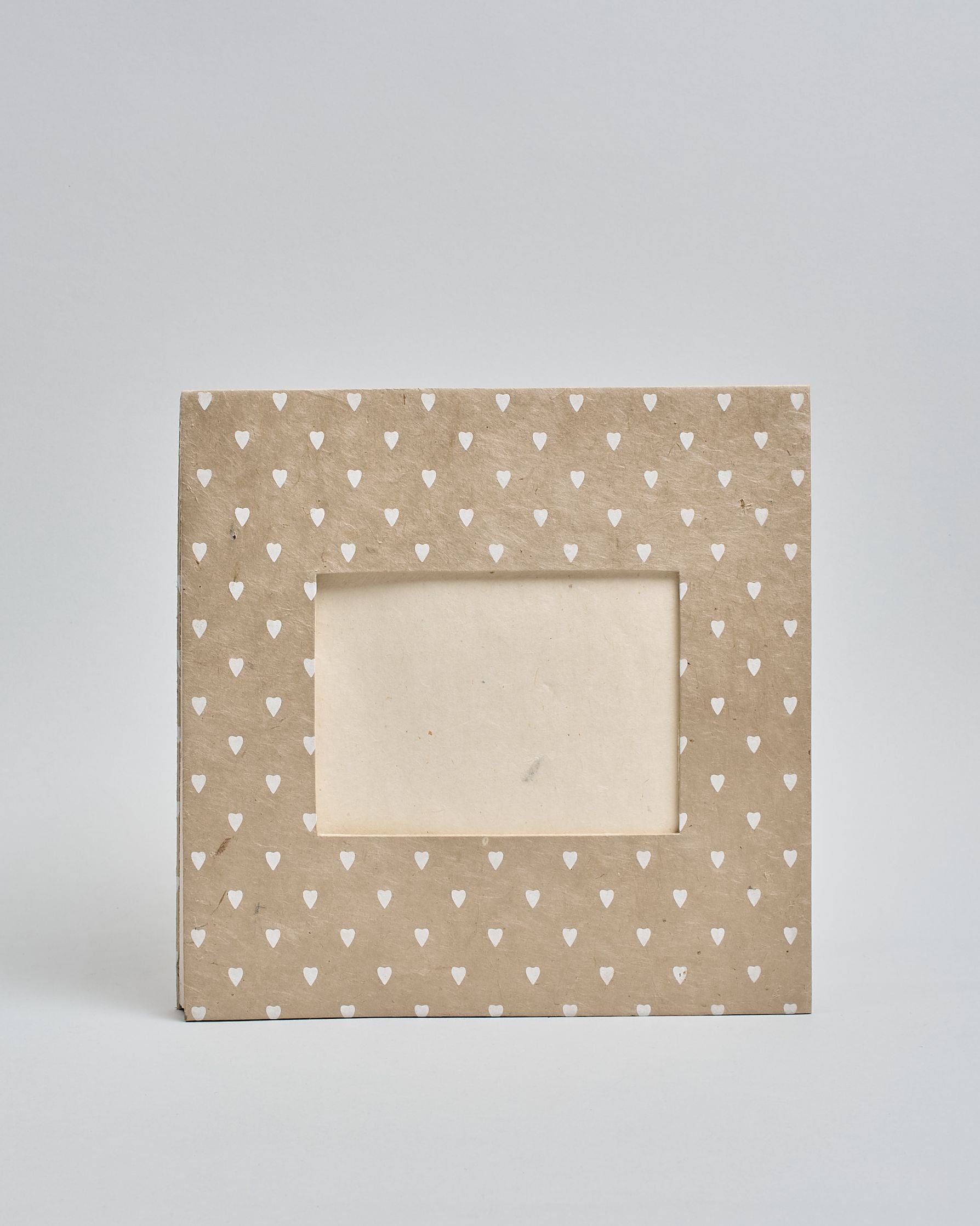 Ein Quadratisches Fotoalbum oder Gästebuch mit Hardcover in beiger Grundfarbe und darauf weiße Herzen, die über das ganze Cover verteilt sind. In der Mitte befindet sich ein rechteckeiges Fenster hinter dem man ein Einlageblatt mit kalligrafiertem Text befestigen kann. #2