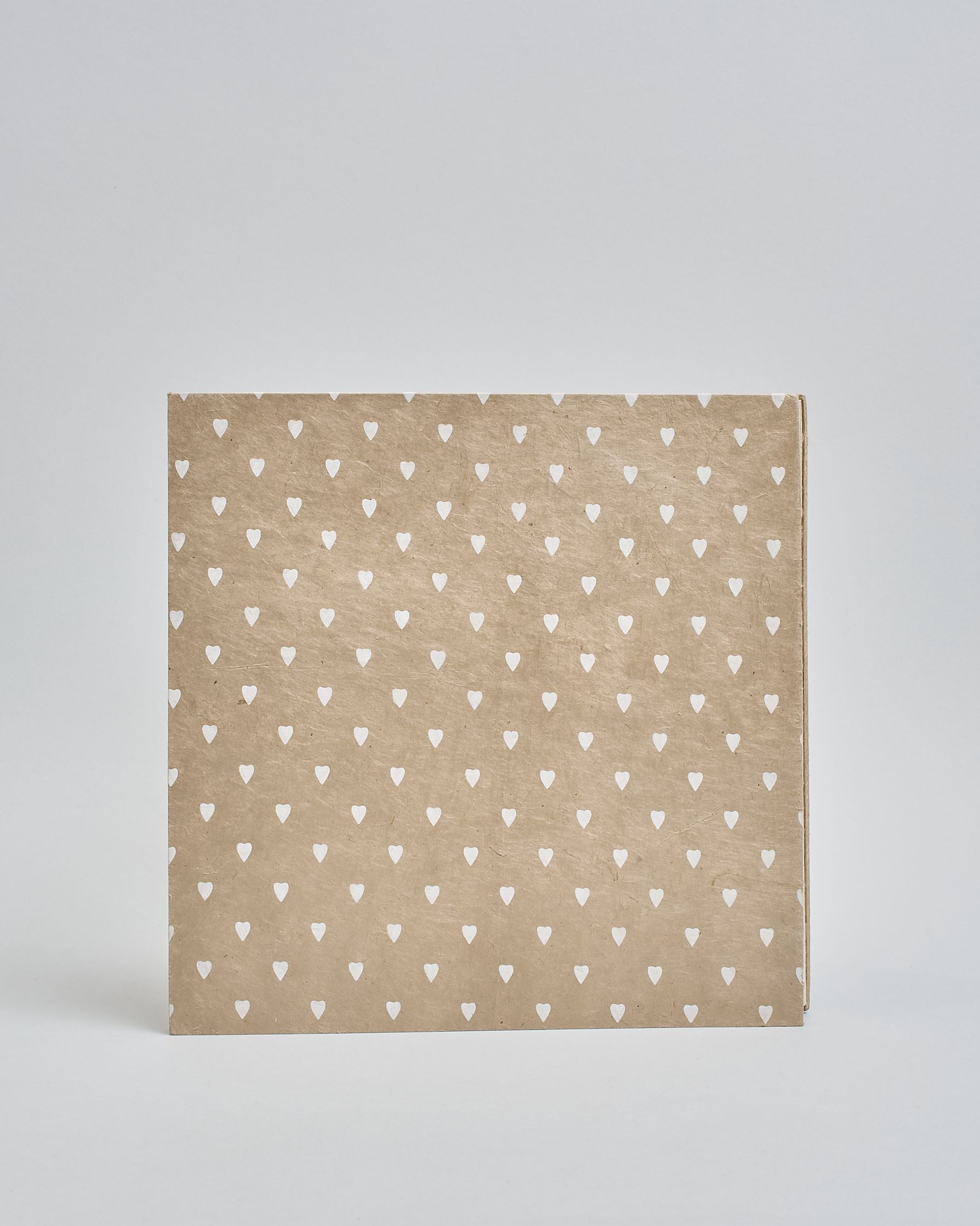 Ein Quadratisches Fotoalbum oder Gästebuch mit Hardcover in beiger Grundfarbe und darauf weiße Herzen, die über das ganze Cover verteilt sind. In der Mitte befindet sich ein rechteckeiges Fenster hinter dem man ein Einlageblatt mit kalligrafiertem Text befestigen kann. #3