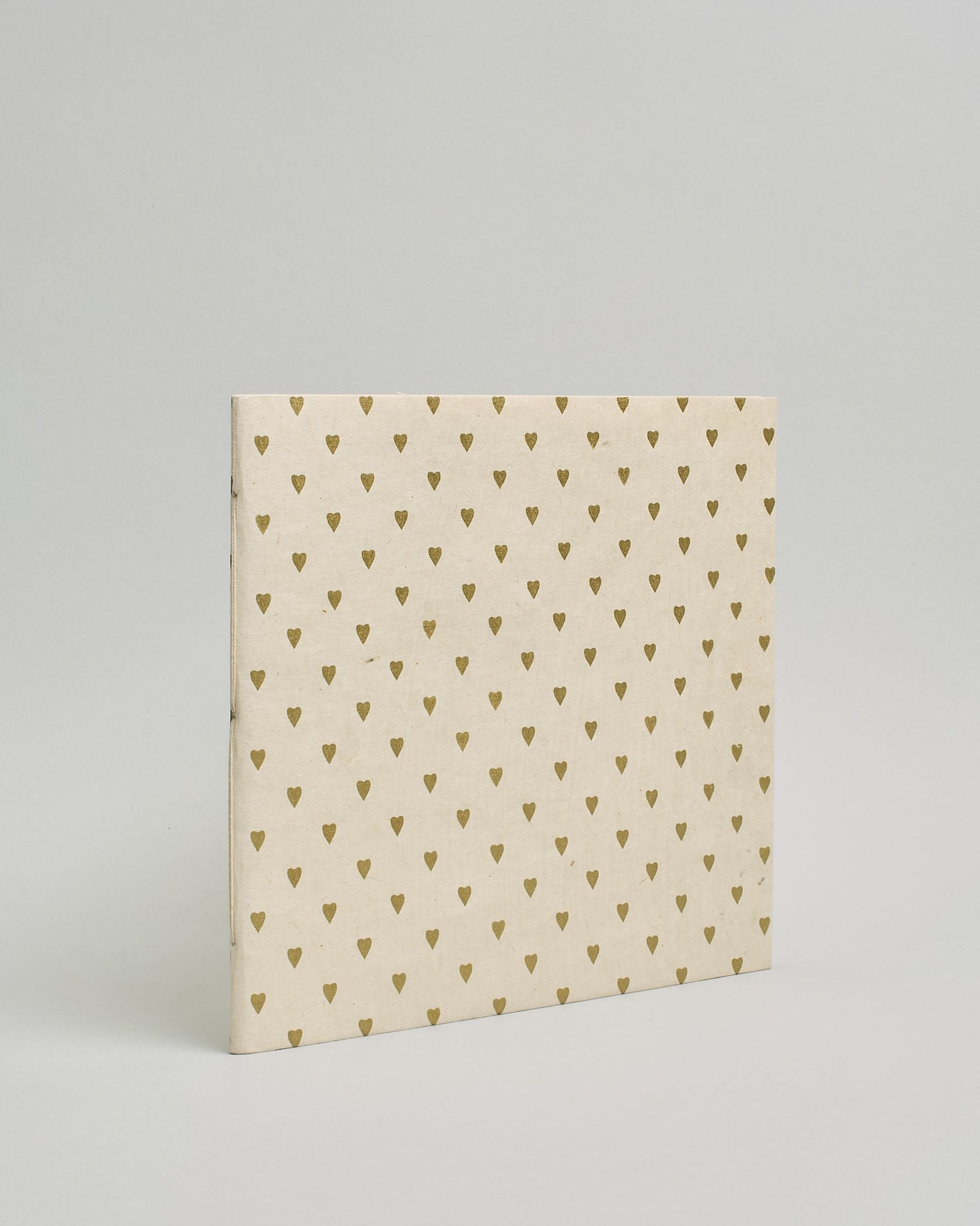 Ein Quadratisches Fotoalbum oder Gästebuch mit Softcover in naturweißer Grundfarbe und darauf goldene kleine Herzen, die über das ganze Cover verteilt sind. #1