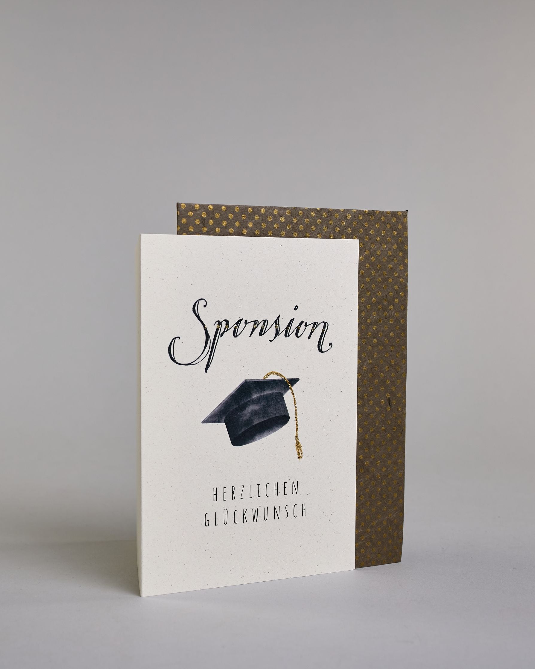 Glückwunschkarte zur Sponsion mit schwarzer Kalligrafieaufschrift ‚Sponsion‘, darunter ein schwarzer Doktorhut mit goldener Quaste und der Text ‚Herzlichen Glückwunsch‘ auf hellem Hintergrund. Dazu ein grün-goldenes handgeschöpftes Kuvert. #3
