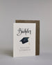 Glückwunschkarte zum Bachelor mit schwarzer Kalligrafieaufschrift ‚Bachelor‘, darunter ein schwarzer Doktorhut mit goldener Quaste und der Text ‚Herzlichen Glückwunsch‘ auf hellem Hintergrund. Dazu ein grün-goldenes handgeschöpftes Kuvert. #3