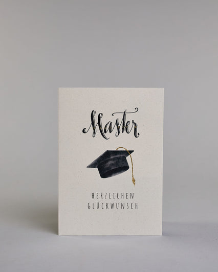 Glückwunschkarte zum Master mit schwarzer Kalligrafieaufschrift ‚Master‘, darunter ein schwarzer Doktorhut mit goldener Quaste und der Text ‚Herzlichen Glückwunsch‘ auf hellem Hintergrund. Dazu ein grün-goldenes handgeschöpftes Kuvert. #1