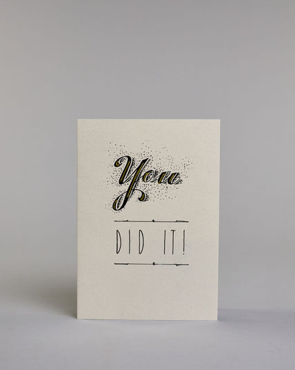 Glückwunschkarte mit schwarzer Kalligrafieaufschrift ‚You did it!‘ ‚YOU‘ mit geschwungener schwarzer Kalligrafieaufschrift gesprenkelten Pünktchen umgeben und Goldverzierung‚ darunter ‚DID IT!‘ mit gerader schwarzer Kalligrafieaufschrift und horizontaler Linie über und unter der Aufschrift auf hellem Hintergrund. Dazu ein gold-weißes handgeschöpftes Kuvert. #1