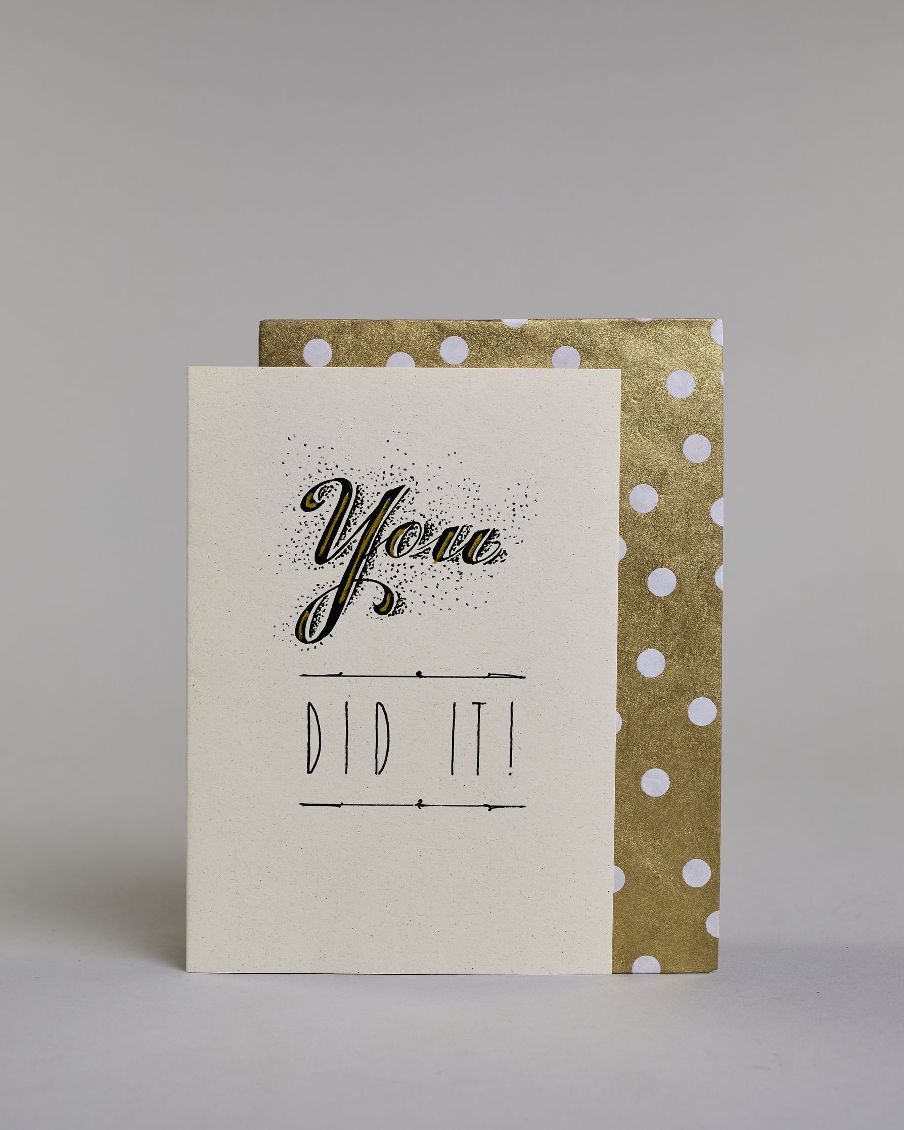 Glückwunschkarte mit schwarzer Kalligrafieaufschrift ‚You did it!‘ ‚YOU‘ mit geschwungener schwarzer Kalligrafieaufschrift gesprenkelten Pünktchen umgeben und Goldverzierung‚ darunter ‚DID IT!‘ mit gerader schwarzer Kalligrafieaufschrift und horizontaler Linie über und unter der Aufschrift auf hellem Hintergrund. Dazu ein gold-weißes handgeschöpftes Kuvert. #2