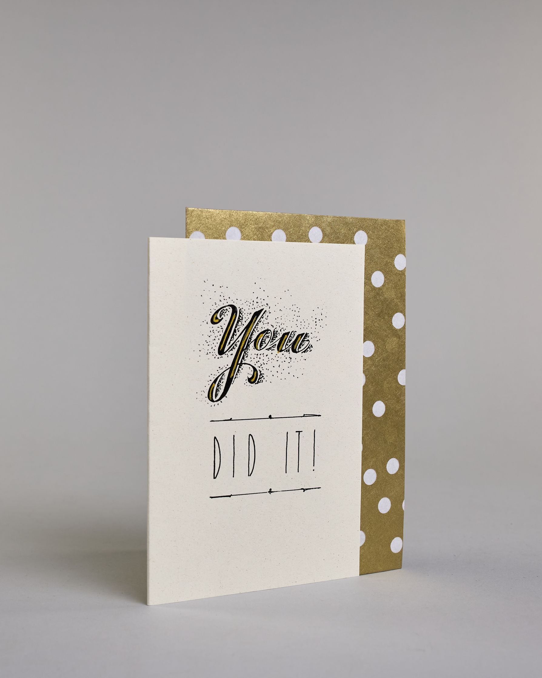 Glückwunschkarte mit schwarzer Kalligrafieaufschrift ‚You did it!‘ ‚YOU‘ mit geschwungener schwarzer Kalligrafieaufschrift gesprenkelten Pünktchen umgeben und Goldverzierung‚ darunter ‚DID IT!‘ mit gerader schwarzer Kalligrafieaufschrift und horizontaler Linie über und unter der Aufschrift auf hellem Hintergrund. Dazu ein gold-weißes handgeschöpftes Kuvert. #3
