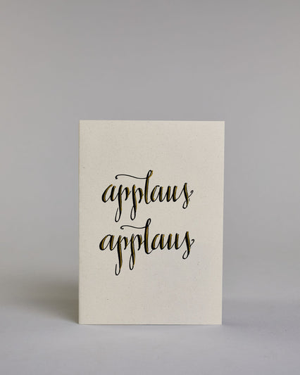 Glückwunschkarte mit schwarzer Kalligrafieaufschrift ‚applaus applaus‘, übereinander geschrieben, Goldverzierung auf hellem Hintergrund. Dazu ein gold-weißes handgeschöpftes Kuvert. #1