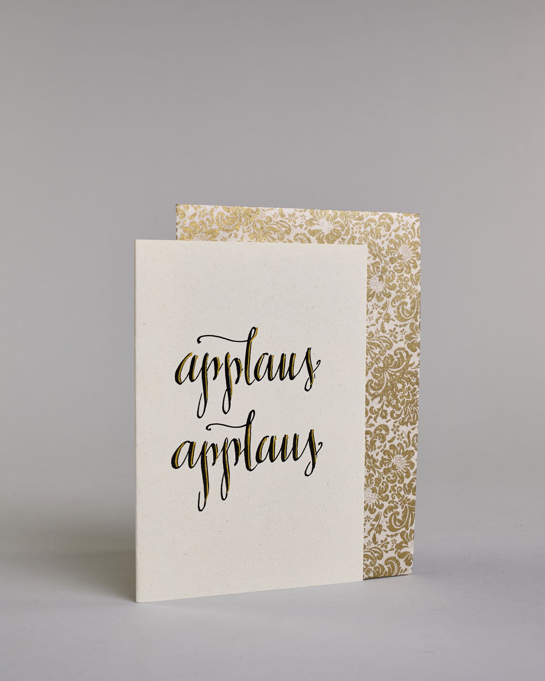 Glückwunschkarte mit schwarzer Kalligrafieaufschrift ‚applaus applaus‘, übereinander geschrieben, Goldverzierung auf hellem Hintergrund. Dazu ein gold-weißes handgeschöpftes Kuvert. #3