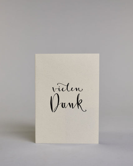 Dankeskarte mit geschwungener schwarzer Kalligrafieaufschrift ‚vielen‘, darunter der Text ‚Dank‘ auf hellem Hintergrund. Dazu ein grün-goldenes handgeschöpftes Kuvert. #1