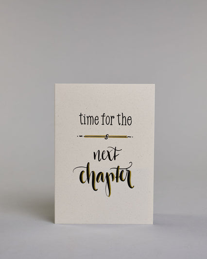 Glückwunschkarte zum Abschied nehmen, auf Englisch mit dem Text ‚time for the next chapter‘. Mit schwarzer Kalligrafieaufschrift ‚time for the‘, darunter eine kunstvolle horizontale Linie, darunter ‚next‘, darunter ‚chapter‘ auf hellem Hintergrund. Dazu ein grün-goldenes Kuvert. #1