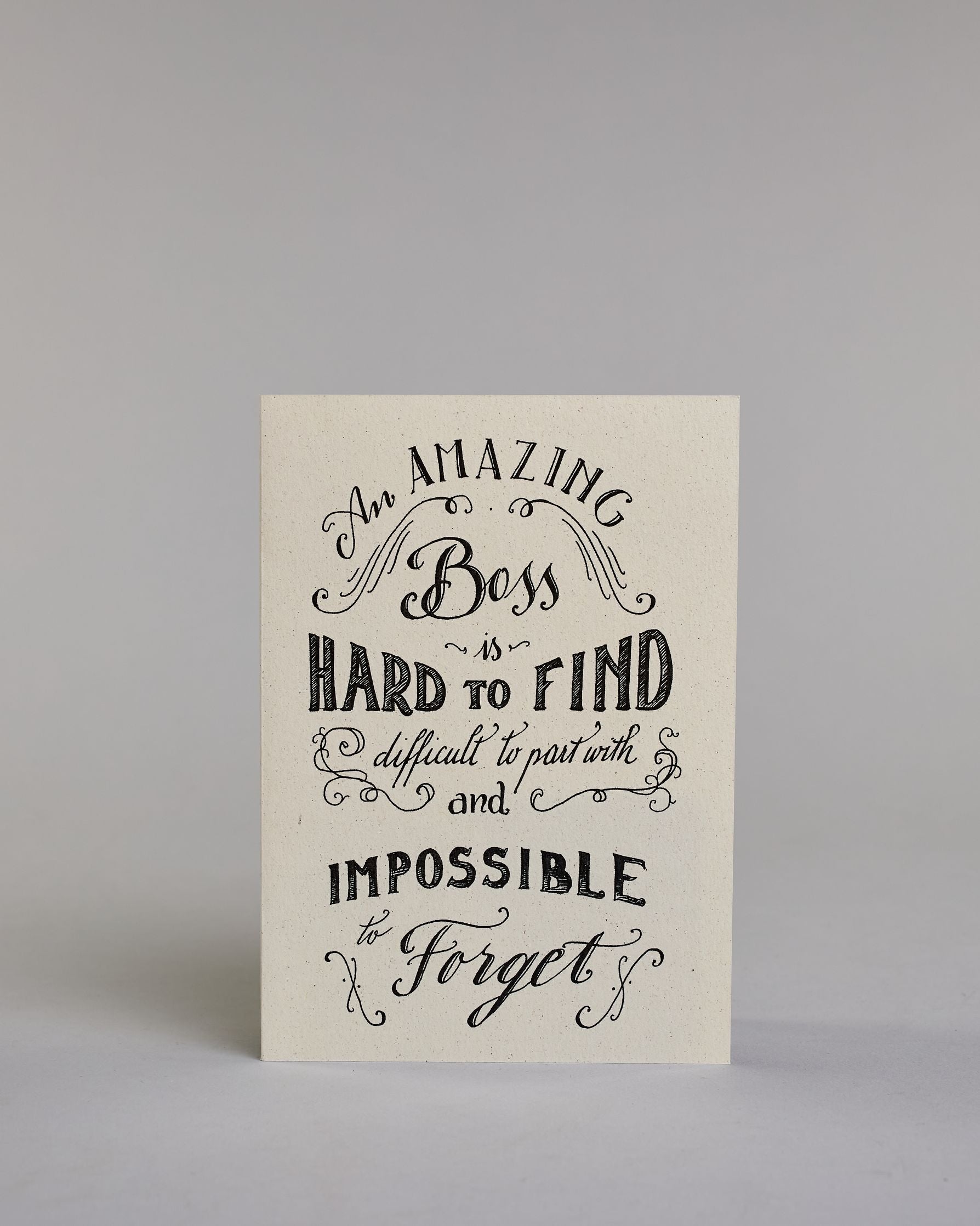 Karte für den Vorgesetzten/ die Vorgesetzte auf Englisch, mit dem Text ‚An amazing Boss is hard to find difficult to part with and impossible to forget‘. Aufgeteilt in folgende Zeilen: ‚An AMAZING‘, darunter ‚Boss‘ umgeben von kunstvollen Verzierungen, darunter ‚is‘, darunter ‚HARD TO FIND‘, darunter ‚difficult to part with‘ umgeben von kunstvollen Verzierungen, darunter ‚and‘, darunter ‚IMPOSSIBLE‘, darunter ‚to Forget‘ umgeben von kunstvollen Verzierungen in unterschiedlichen Kalligrafieaufschriften auf…