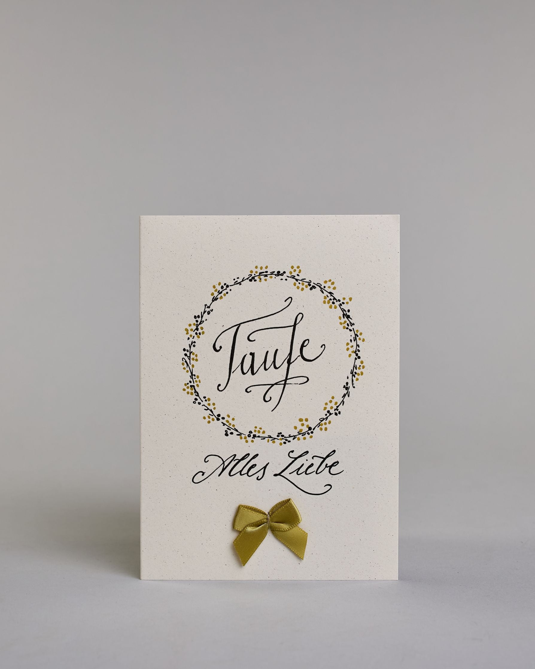 Glückwunschkarte zur Taufe mit geschwungener schwarzer Kalligrafieaufschrift in gezeichnetem Kranz ‚Taufe‘, darunter der Text ‚Alles Liebe‘, darunter eine aufgenähte goldene Masche auf hellem Hintergrund. Dazu ein weiß-goldenes handgeschöpftes Kuvert. #1
