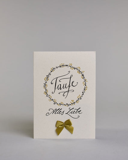 Glückwunschkarte zur Taufe mit geschwungener schwarzer Kalligrafieaufschrift in gezeichnetem Kranz ‚Taufe‘, darunter der Text ‚Alles Liebe‘, darunter eine aufgenähte goldene Masche auf hellem Hintergrund. Dazu ein weiß-goldenes handgeschöpftes Kuvert. #1