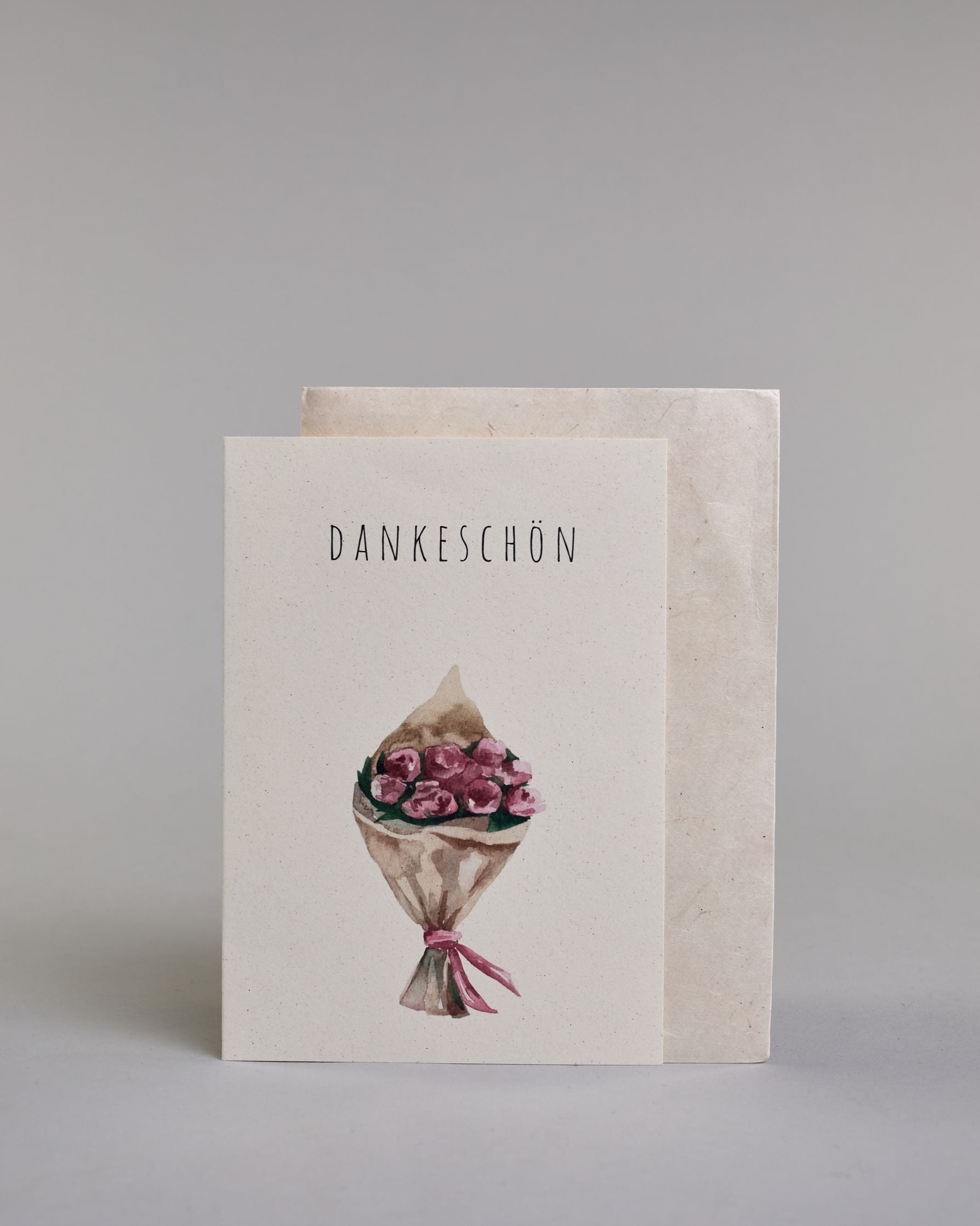 Dankeskarte mit dünner, gerader, schwarzer Kalligrafieaufschrift  ‚DANKESCHÖN‘,  darunter ein gezeichneter Blumenstrauß auf hellem Hintergrund. Dazu ein weißes handgeschöpftes Kuvert. #2