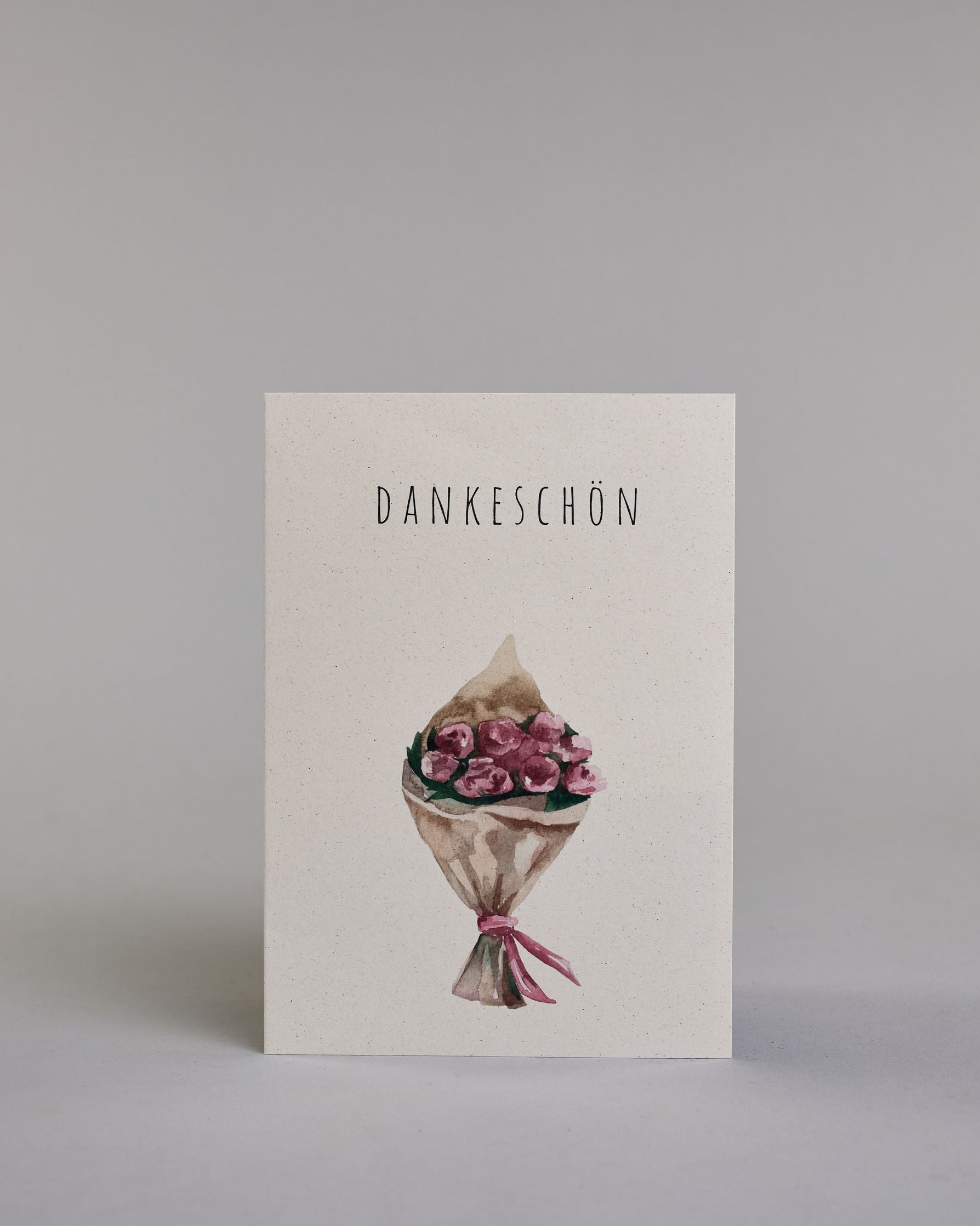Dankeskarte mit dünner, gerader, schwarzer Kalligrafieaufschrift  ‚DANKESCHÖN‘,  darunter ein gezeichneter Blumenstrauß auf hellem Hintergrund. Dazu ein weißes handgeschöpftes Kuvert. #1