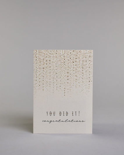 Allgemeine Glückwunschkarte auf Englisch mit schwarzer Kalligrafieaufschrift ‚You did it! Congratulations‘, von oben kommt ein Goldregen bis zu Hälfte der Karte, darunter in dünner, gerader Kalligrafieaufschrift ‚YOU DID IT!‘, darunter in geschwungener Kalligrafieaufschrift ‚congratulations‘ aufs hellem Hintergrund. Dazu ein gold-weißes handgeschöpftes Kuvert. #1