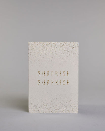 Karte in Englisch mit goldener Kalligrafieaufschrift ‚surprise surprise‘, von der oberen und unteren Kartenkante kommt ein Pünktchenregen auf hellem Hintergrund. Dazu ein weißes handgeschöpftes Kuvert. #1
