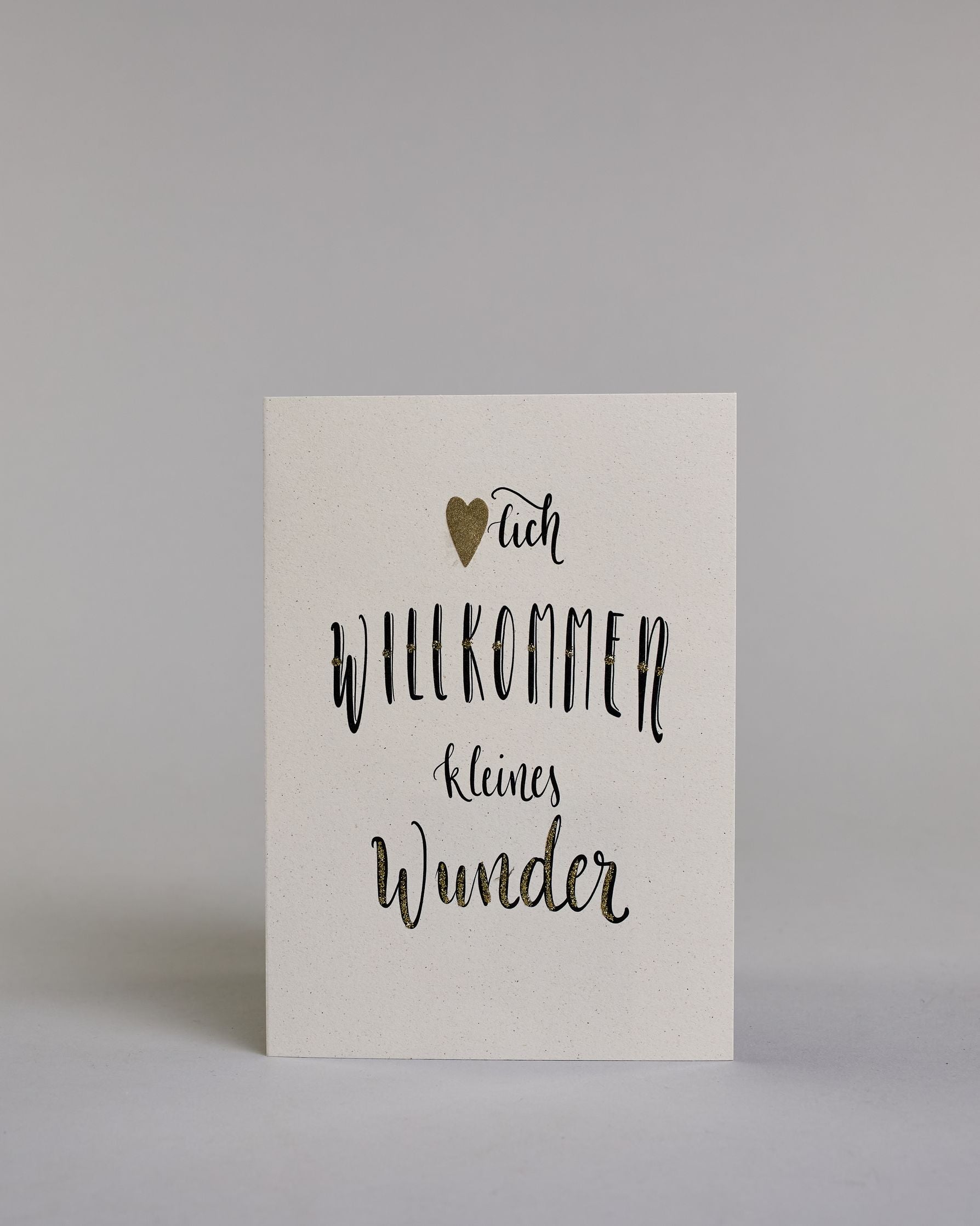 Glückwunschkarte zur Geburt mit der Aufschrift „Herzlich willkommen kleine Wunder“ in schwarzer Kalligrafieaufschrift, wobei in dem Wort „Herzlich" das "Herz" durch ein aufgeklebtes goldenes Herz ersetzt wurde. Das Wort „Wunder“ ist mit goldfarbenen Details verziert. Über dem Wort „Prinz“ ist eine kleine goldene Krone abgebildet. Dazu ein gold-weißes handgeschöpftes Kuvert. #1