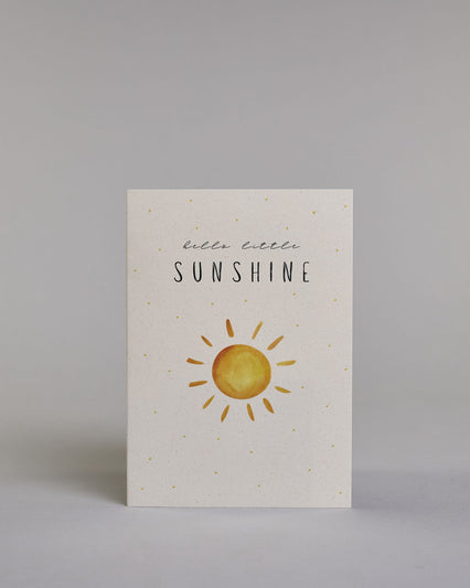 Glückwunschkarte zur Geburt in Englisch mit der Aufschrift „hello little SUNSHINE“ in schwarzer Handlettering-Schrift. Das "hello little" ist in geschwungener Kalligrafieschrift, darunter das"Sunshine" in dünner gerader Schrift. Darunter ist eine gezeichnete gelb-orangefarbene Sonne mit Strahlen. Der Hintergrund ist hell mit kleinen goldenen Punkten. Dazu ein beige-weißes handgeschöpftes Kuvert. #1