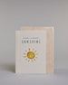 Glückwunschkarte zur Geburt in Englisch mit der Aufschrift „hello little SUNSHINE“ in schwarzer Handlettering-Schrift. Das "hello little" ist in geschwungener Kalligrafieschrift, darunter das"Sunshine" in dünner gerader Schrift. Darunter ist eine gezeichnete gelb-orangefarbene Sonne mit Strahlen. Der Hintergrund ist hell mit kleinen goldenen Punkten. Dazu ein beige-weißes handgeschöpftes Kuvert. #2