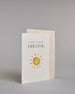 Glückwunschkarte zur Geburt in Englisch mit der Aufschrift „hello little SUNSHINE“ in schwarzer Handlettering-Schrift. Das "hello little" ist in geschwungener Kalligrafieschrift, darunter das"Sunshine" in dünner gerader Schrift. Darunter ist eine gezeichnete gelb-orangefarbene Sonne mit Strahlen. Der Hintergrund ist hell mit kleinen goldenen Punkten. Dazu ein beige-weißes handgeschöpftes Kuvert. #3