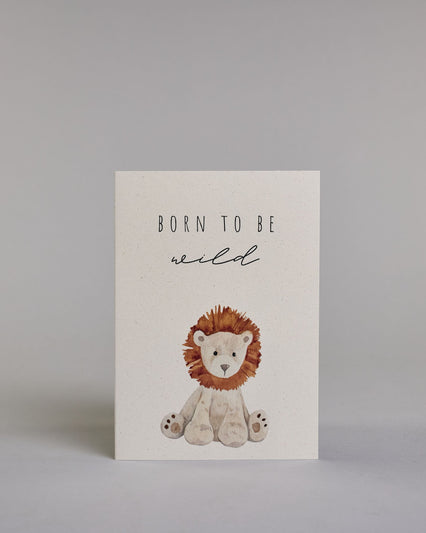 Glückwunschkarte zur Geburt in Englisch mit der Aufschrift „Born to be wild“ in schwarzer Handlettering-Schrift. Das "Born to be" ist in gerader Kalligrafieaufschrift, darunter das "wild" in geschwungener Schrift dargestellt. Darunter ist ein gezeichneter Stofftier-Löwe mit brauner Mähne und hellbeigem Fell abgebildet. Dazu ein beige-weißes handgeschöpftes Kuvert. #1