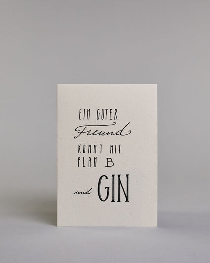 Karte mit der Aufschrift „Ein guter Freund kommt mit Plan B und Gin“ in schwarzer, variierender Handlettering-Schrift auf hellem Hintergrund. Die Zeilen setzten sich wiefolgt zusammen: "Ein guter" in gerader Schrift, darunter "Freund" in geschwungener Schrift, darunter "KOMMT MIT" in gerader Schrift, darunter "PLAN B" in gerader Schrift, darunter "und GIN". Dazu ein grün-goldenes handgeschöpftes Kuvert. #1